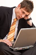 Zmartwiony biznesman wpatruje się w laptop po przegranej podpierając głowę