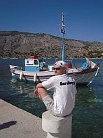 szachinista w koszulce SureBety.pl na tle greckiej łódki i gór