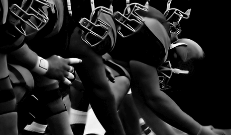 Czarno białe zdjęcie futbolistów amerykańskich ustawionych w jednej linii przed rozpoczęciem gry