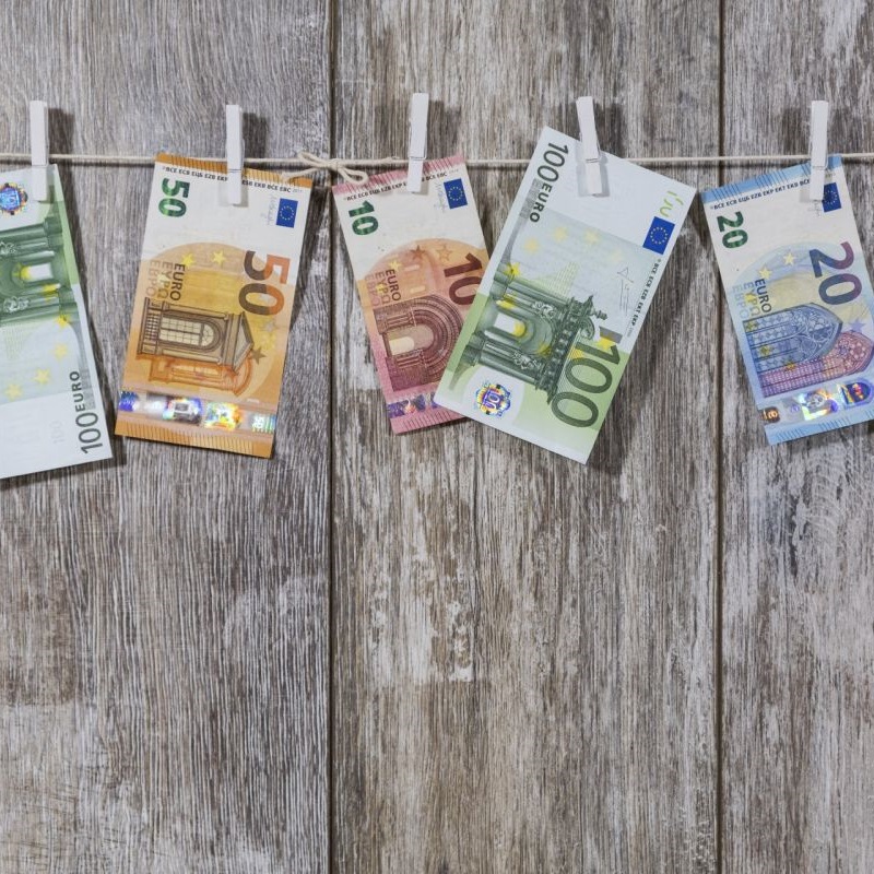 Banknoty 10 20 50 i 100 euro powieszone spinaczami na sznurku na tle drewnianych desek