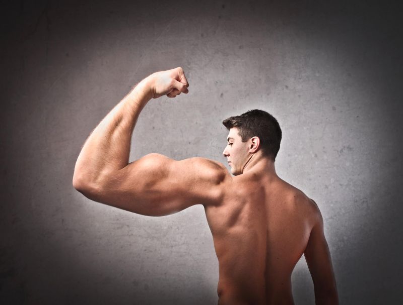 Góra nagiego mężczyzny który pręży nieproporcjonalnie duży lewy biceps na ciemnoszarym tle