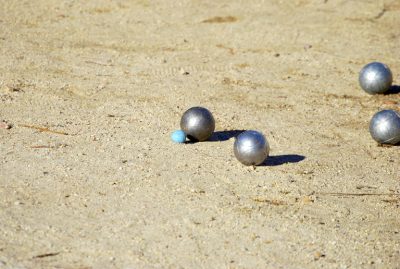 Duża metalowa kula na piasku leży bliżej małej niebieskiej kulki niż druga metalowa kula obok