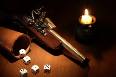 Mroczne zdjęcie starodawnego pistoletu na stole w towarzystwie świecy i pięciu kostek do gry wysypanych z kubka
