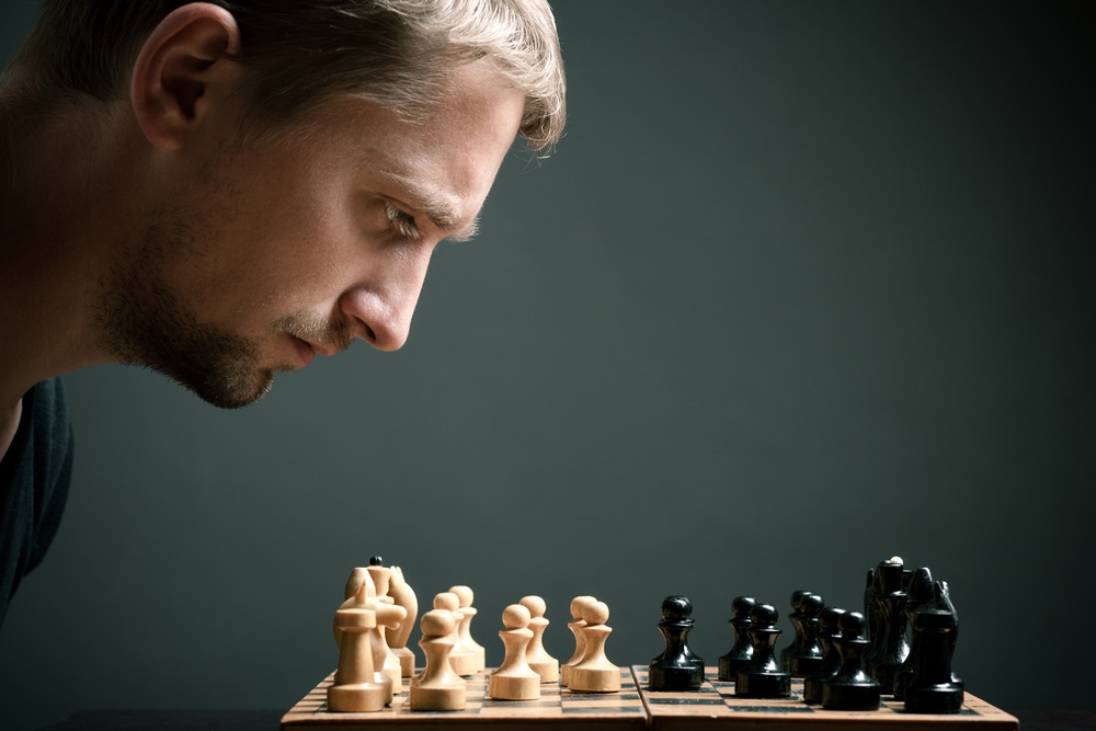 Głowa mężczyzny spogląda na szachownicę z wysuniętymi pionami obu stron do centrum