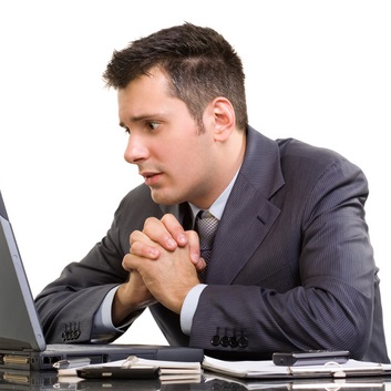 Mężczyzna siedzi wpatrzony w laptop ze splecionymi dłońmi w geście prośby i strachem w oczach