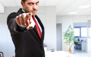 Mężczyzna w garniturze wskazuje na ciebie palcem z surową miną na tle biura firmy
