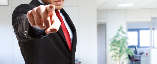 Mężczyzna w garniturze wskazuje na ciebie palcem z surową miną na tle biura firmy