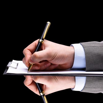 Dłoń mężczyzny w garniturze na lustrzanym blacie podpisuje czarnym długopisem papierową notatkę
