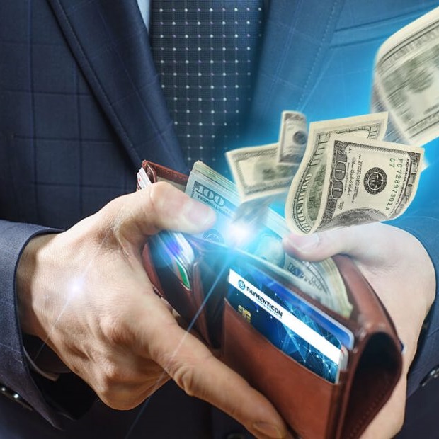 Zbliżenie na dłonie mężczyzny w garniturze który trzyma przed sobą rozchylony portfel z którego wyfruwają dolary