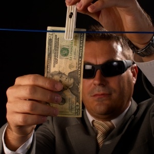 Mężczyzna w garniturze i ciemnych okularach wiesza na sznurku banknot dolarowy
