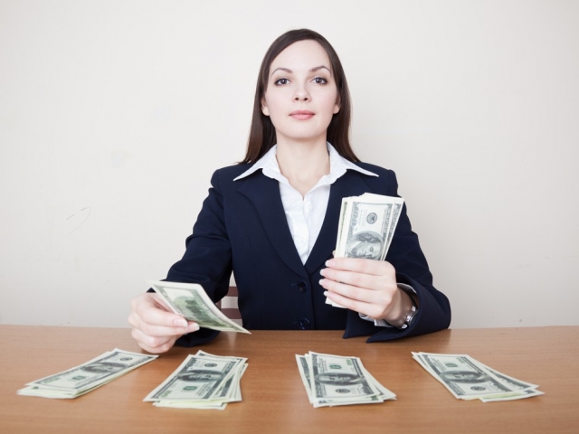 Kobieta w garsonce wykłada cztery równe stosy banknotów na stół