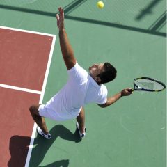 Widok z góry na tenisistę podrzucającego piłeczkę na tle pomarańczowo zielonego kortu