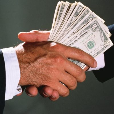Uścisk dłoni mężczyzn w garniturach przekazujący plik banknotów studolarowych