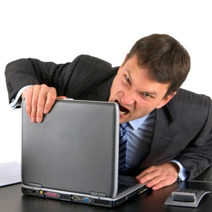 Wściekły biznesmen chce ugryźć przy biurku górną krawędź otworzonego laptopa