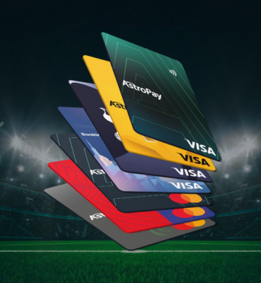 Kilka kart płatniczych ułożonych w wachlarz na tle zachmurzonego boiska piłkarskiego