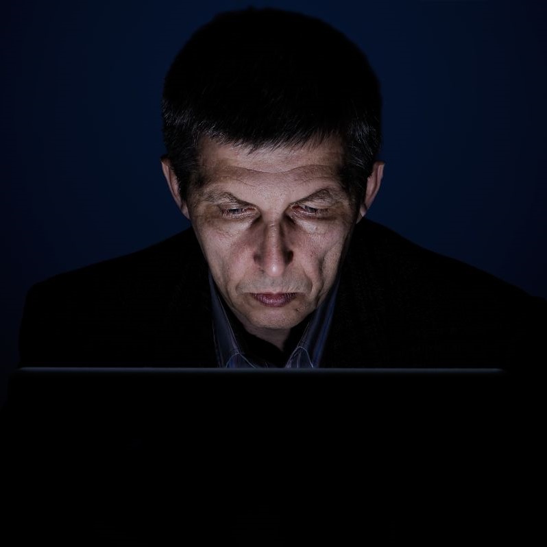 Podświetlona twarz mężczyzny w średnim wieku przed laptopem