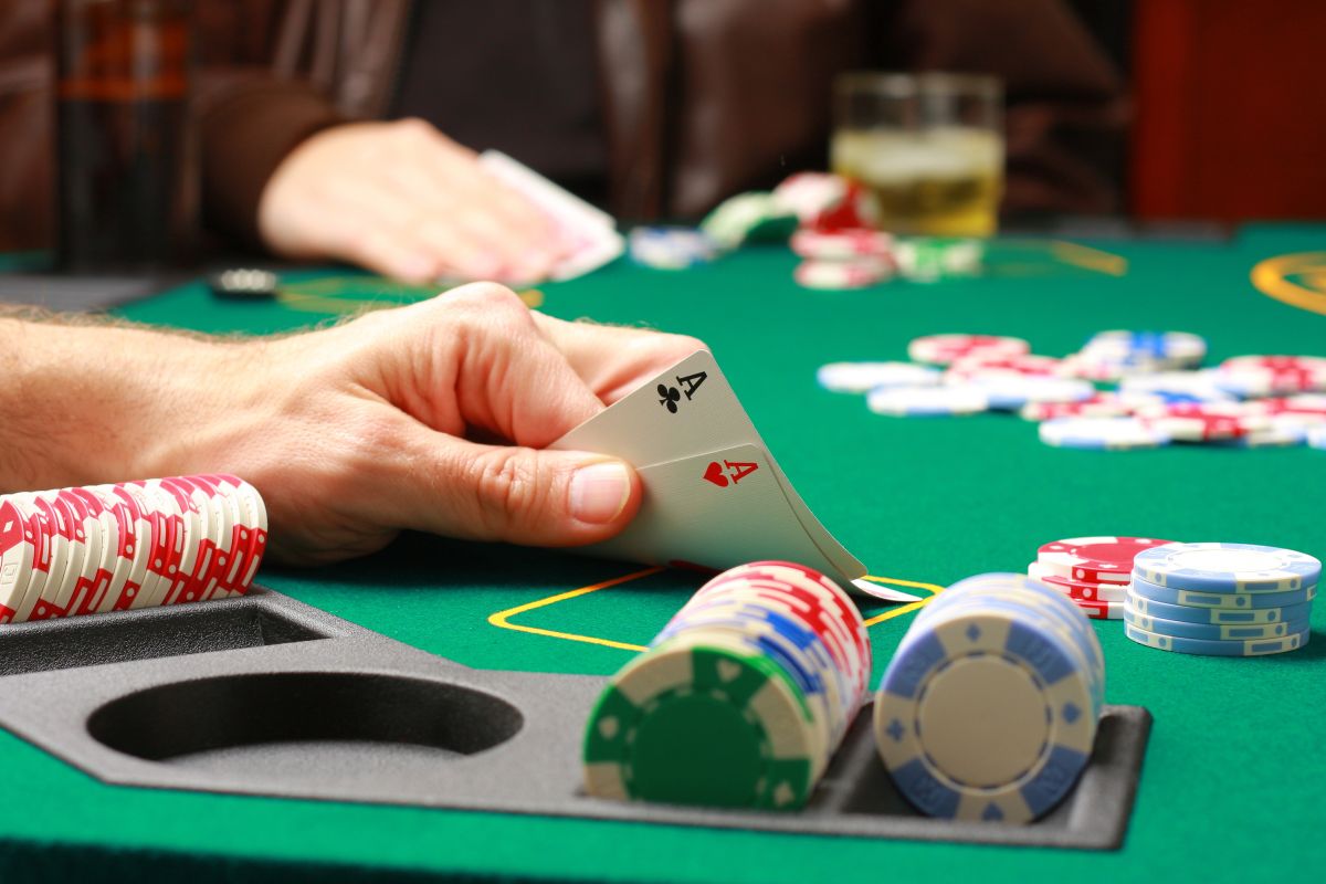 Ręka gracza otoczona żetonami do pokera pokazuje parę asów na zielonym stoliku