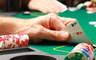 Ręka gracza otoczona żetonami do pokera pokazuje parę asów na zielonym stoliku