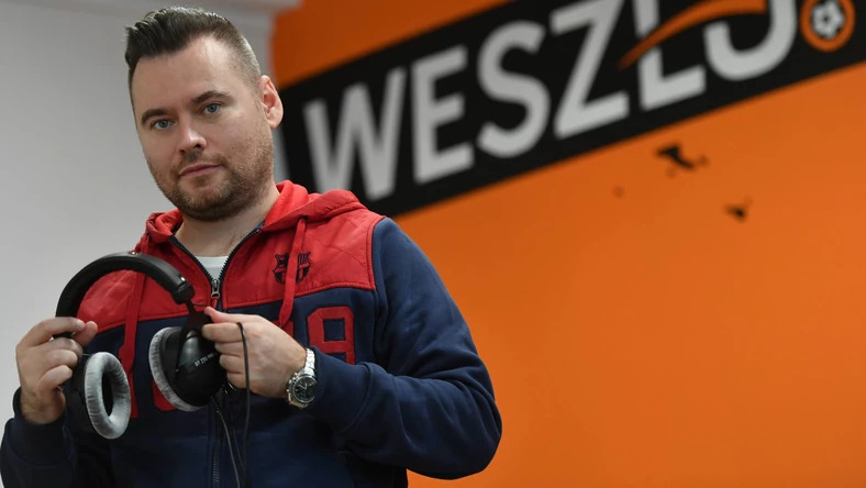 Krzysztof Stanowski trzymający słuchawki na tle logo Weszło.com
