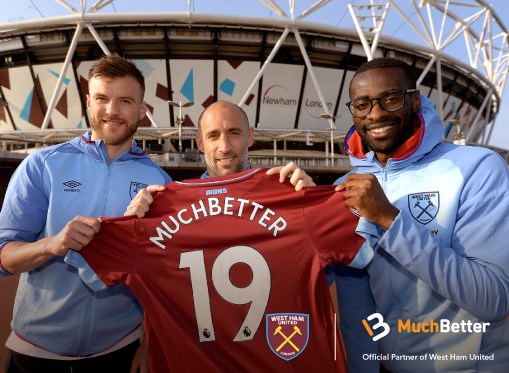 Trzech piłkarzy trzyma koszulkę z napisem Muchbetter na tle stadionu