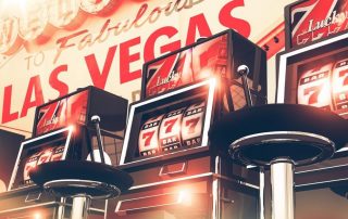Widok z dołu na trzy czerwone automaty przed którymi są okrągłe krzesełka obrotowe a w tle czerwony napis Las Vegas