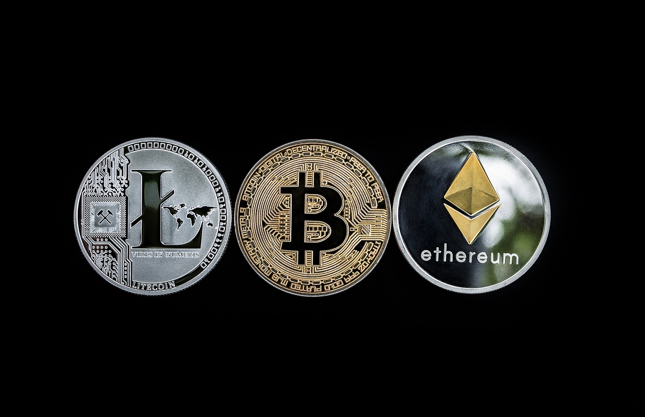 Trzy fizyczne monety na czarnym tle imitujące litecoin bitcoin oraz ethereum